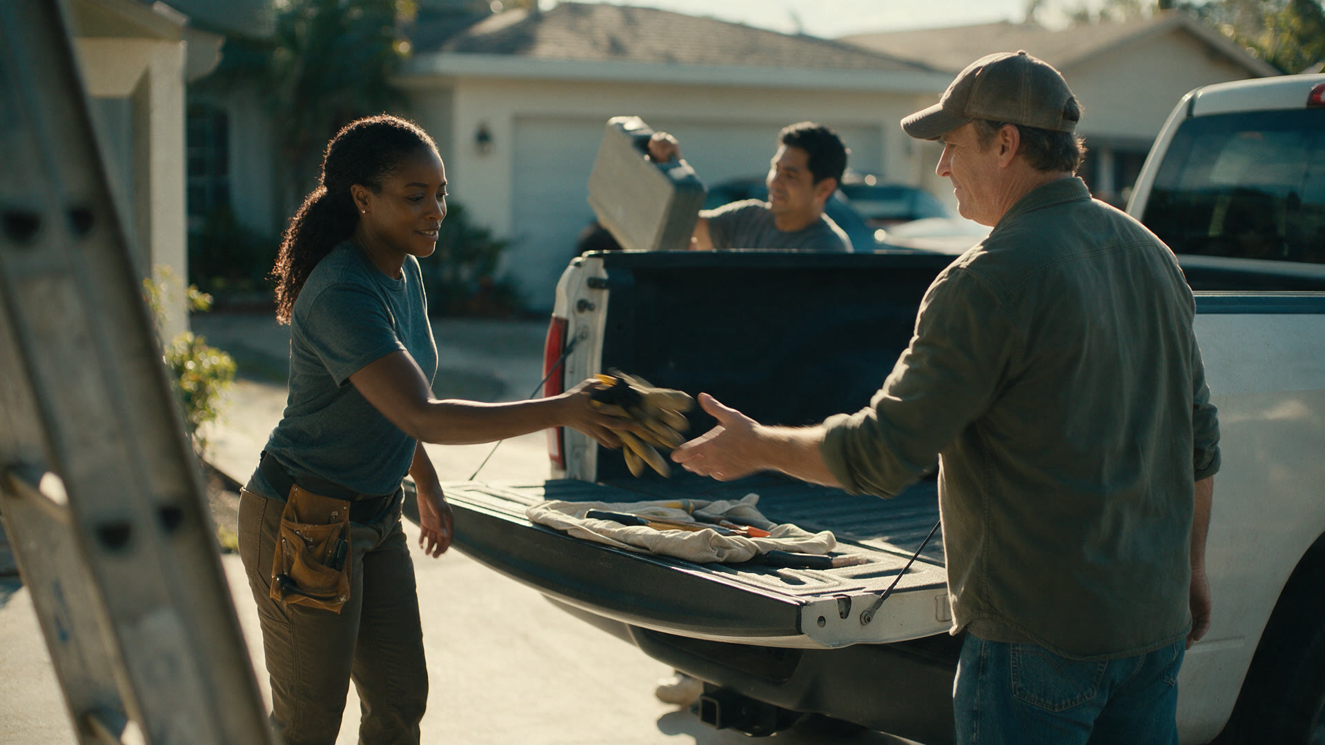 A person hands a pair of gloves to another person at the open tailgate of a pickup truck